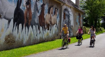 Trois personnes à vélo qui passent à côté d'un mur décoré de cheveux à Murlin